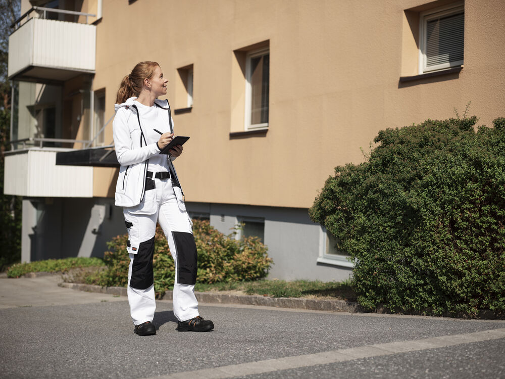 Målare i vita hantverksbyxor och jacka utanför ett flerbostadshus