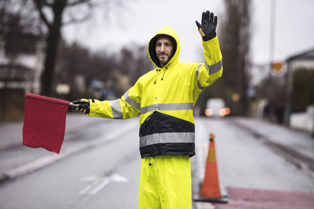 Flaggvakt i gula varselregnkläder vid en kon på gatan