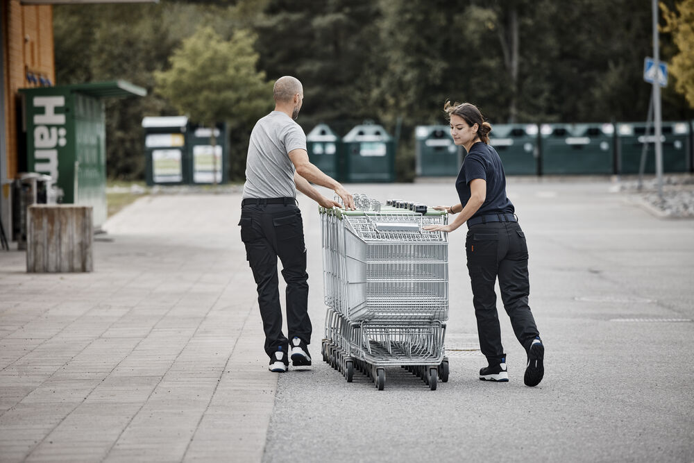 Två personer i servicebyxor drar en vagn utomhus