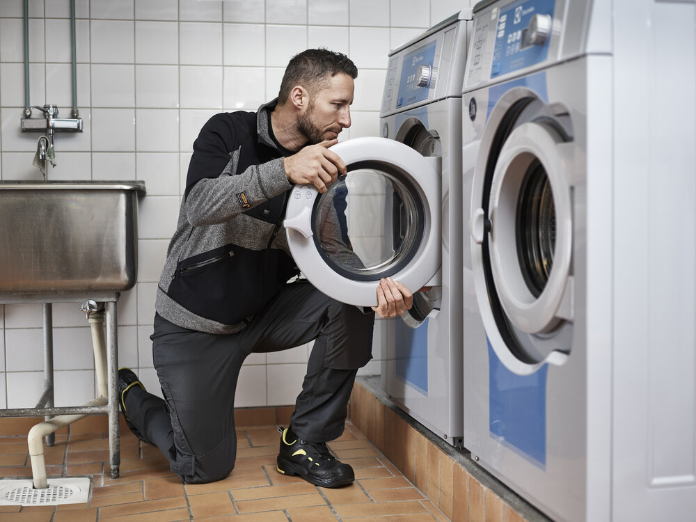 Servicetekniker på knä vid en tvättmaskin